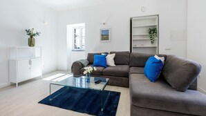A modern living room with a glass coffee table, a grey sofa with blue cushions, a white cabinet, and a bookshelf. - Casa do Vale - in Paderne (Paderne)