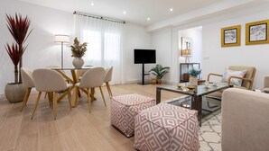 A modern living room with a glass coffee table, a dining area with chairs, a sofa, and a TV. - Luxury Apartment in Cordoba Center. Plaza Doblas (Córdoba)