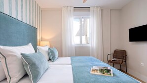 Una camera d'albergo con un letto, una sedia, una televisione e una finestra con tende.
