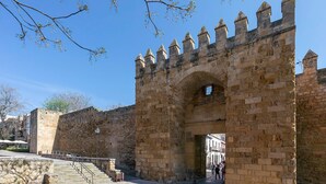 Un'antica porta in pietra con un arco centrale e una scalinata che vi conduce, sotto un cielo azzurro intenso.
