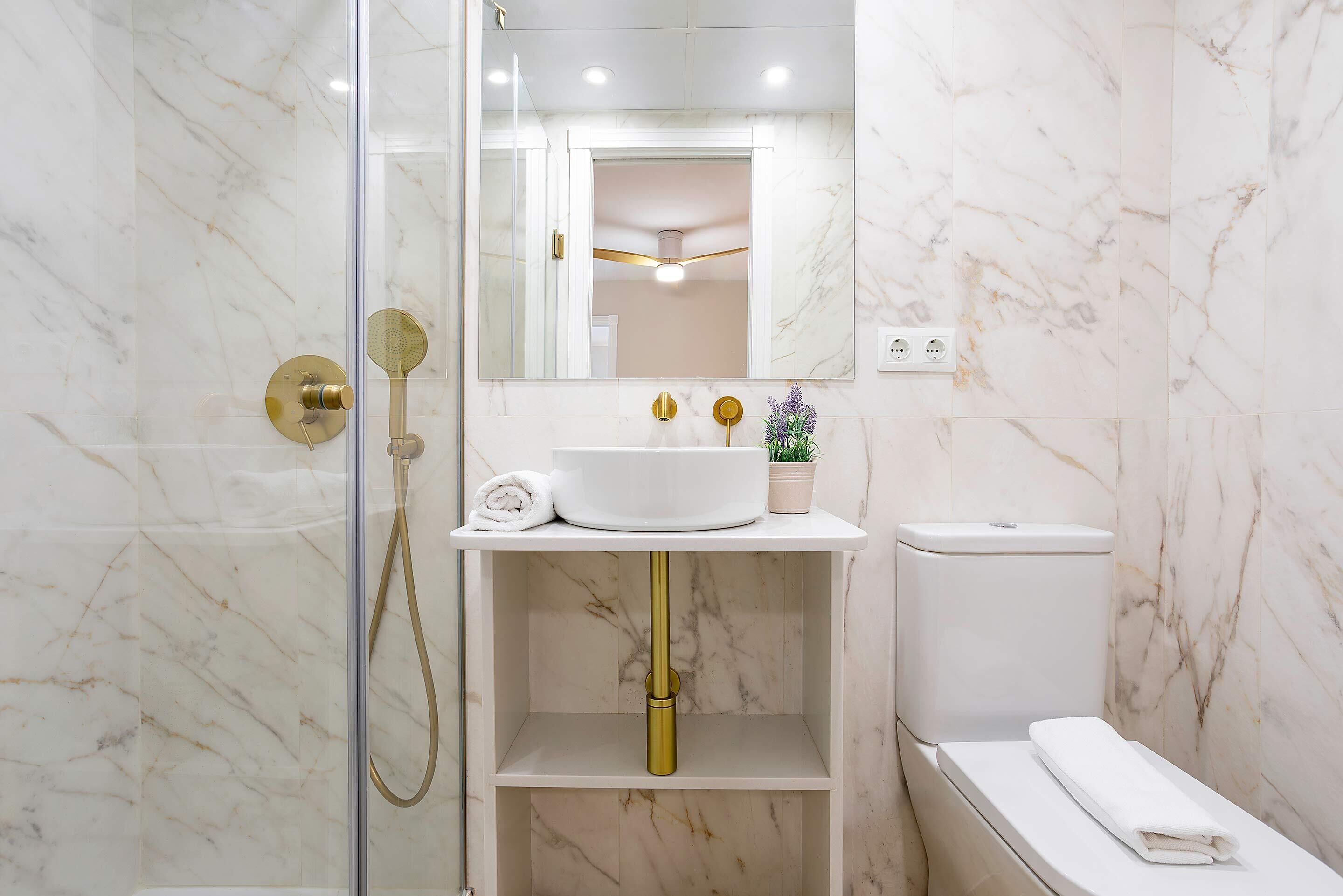Une salle de bain avec une douche à parois de verre, un lavabo blanc avec des robinets dorés et un mur en marbre.