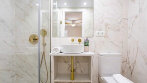 Un bagno con cabina doccia in vetro, un lavabo bianco con accessori dorati e una parete in marmo.