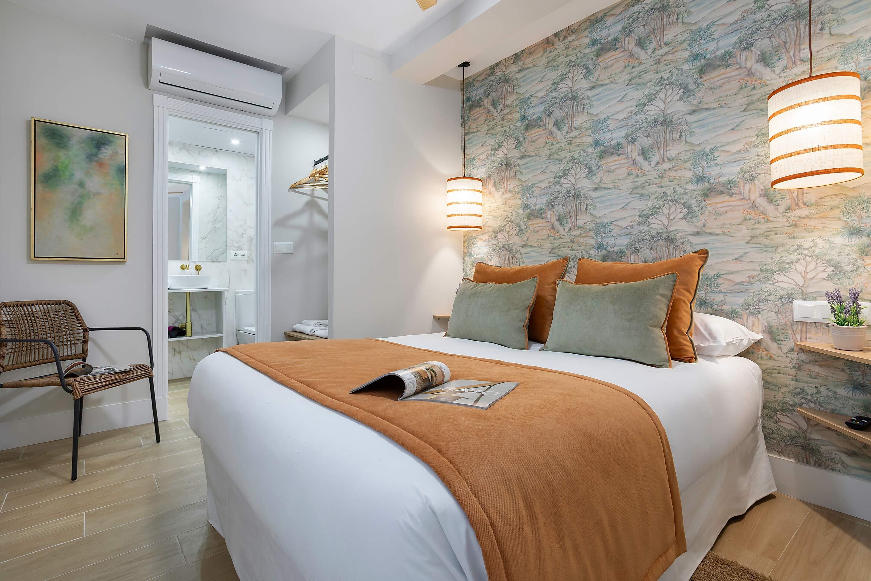 Un dormitorio con cama, una silla, una mesita de noche, aire acondicionado instalado en la pared y un papel tapiz con motivos naturales.