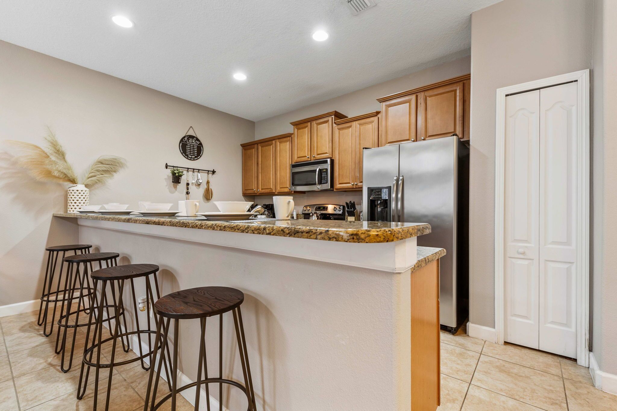 A kitchen with wooden cabinets, a stainless steel refrigerator, a granite countertop, and bar stools.