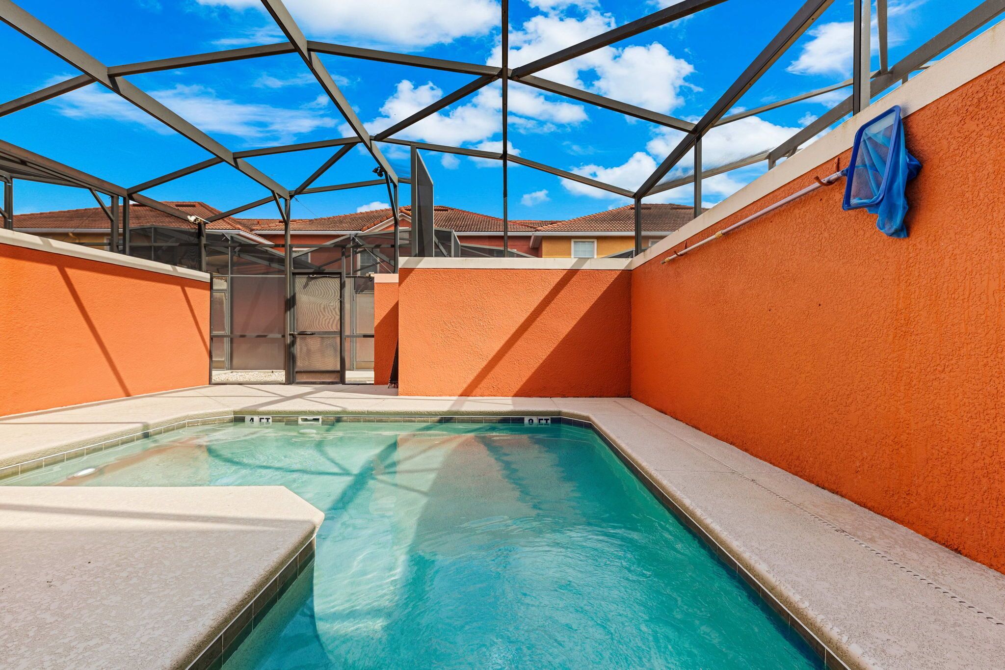 A swimming pool with a glass ceiling, surrounded by orange walls, and a clear blue sky above.