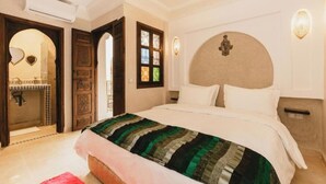 A hotel room with a large bed, a wooden door, a mirror, and a wall-mounted light fixture. - L'Emeraude de la Médina - Eleganza e Comfort nel Cuore di Marrakech (Medina)