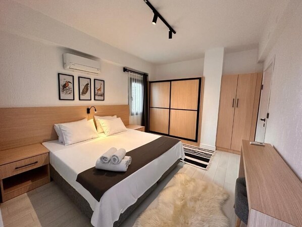 Una habitación de hotel con cama, mesita de noche, armario y un ventanal grande con cortinas.