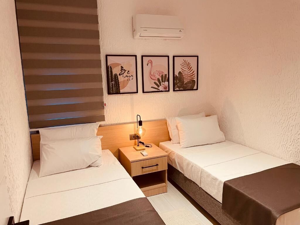 Ein Hotelzimmer mit zwei Betten, einem Nachttisch mit Lampe und drei gerahmten Bildern an der Wand.