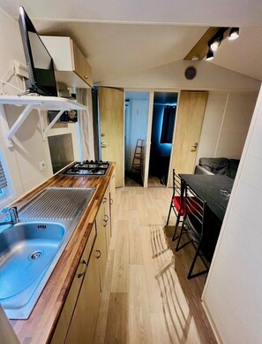 A compact kitchen with a sink, stove, and dining area. - Mobilhome 4 Pers. near beaches + pool (Port-la-Nouvelle)
