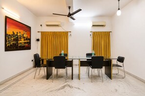 A conference room with a glass table, black chairs, yellow curtains, ceiling fans, and an air conditioning unit. - Next Generation Guest House (Bidhannagar)