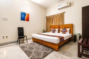 A hotel room with a bed, a chair, a desk, an air conditioner, and a painting on the wall. - Next Generation Guest House (Bidhannagar)