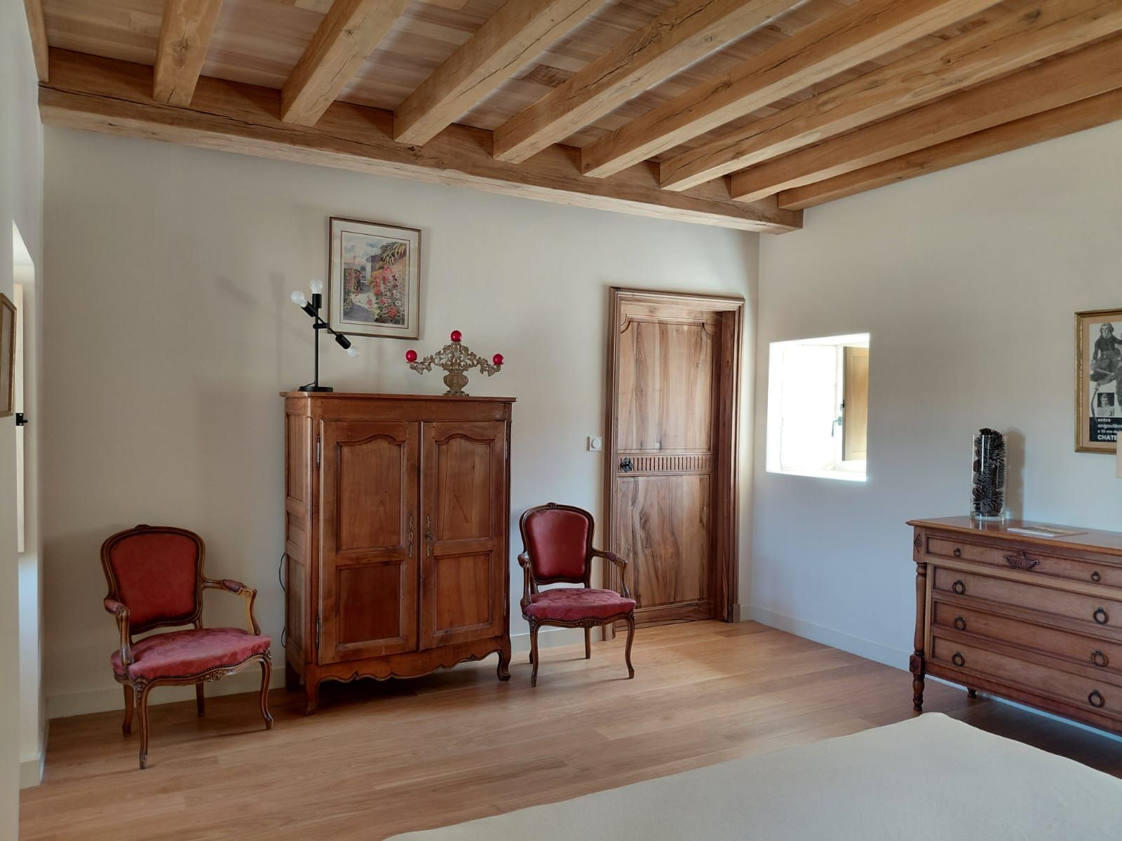 A room with wooden flooring, a large cabinet, two chairs, a door, and a dresser.