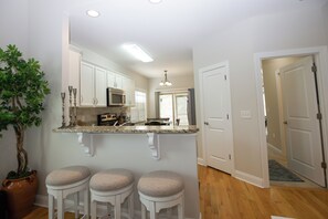 A kitchen with white cabinets, a microwave, and a bar area with stools.
