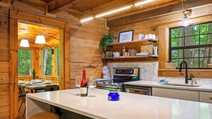 A wooden cabin interior with a kitchen, dining area, and large windows. - Gimme the Smokies, 2 BR, 2 BA, Sleeps 6 (Townsend)