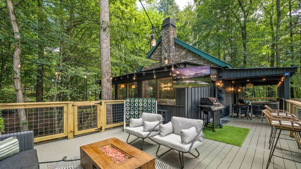 A deck with outdoor seating, a fire pit, and a barbecue area, surrounded by a forest. - Gimme the Smokies, 2 BR, 2 BA, Sleeps 6 (Townsend)