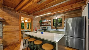 A wooden cabin interior with a kitchen, bar stools, and a stainless steel refrigerator. - Gimme the Smokies, 2 BR, 2 BA, Sleeps 6 (Townsend)