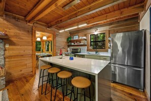 Ein Holzblockhaus-Innenraum mit Küche, Barhocker und einem Edelstahlkühlschrank.