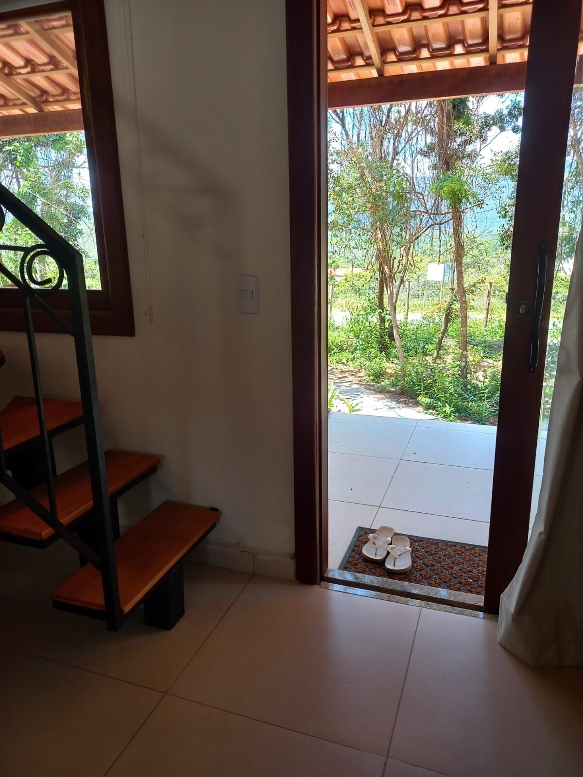 A staircase leading to a covered outdoor area with a view of greenery and a tiled floor.