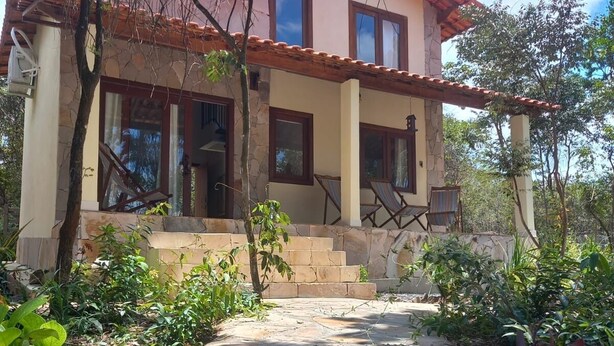 A two-story house with a stone facade, a red-tiled roof, and a covered porch with chairs. - Colibri Chalet in Vale do Capão, Chapada Diamantina, Bahia, with panoramic views. (Caeté-Açu)