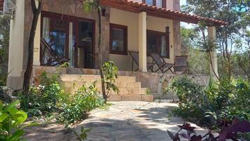 A two-story house with a stone facade, a red-tiled roof, and a covered porch with chairs.