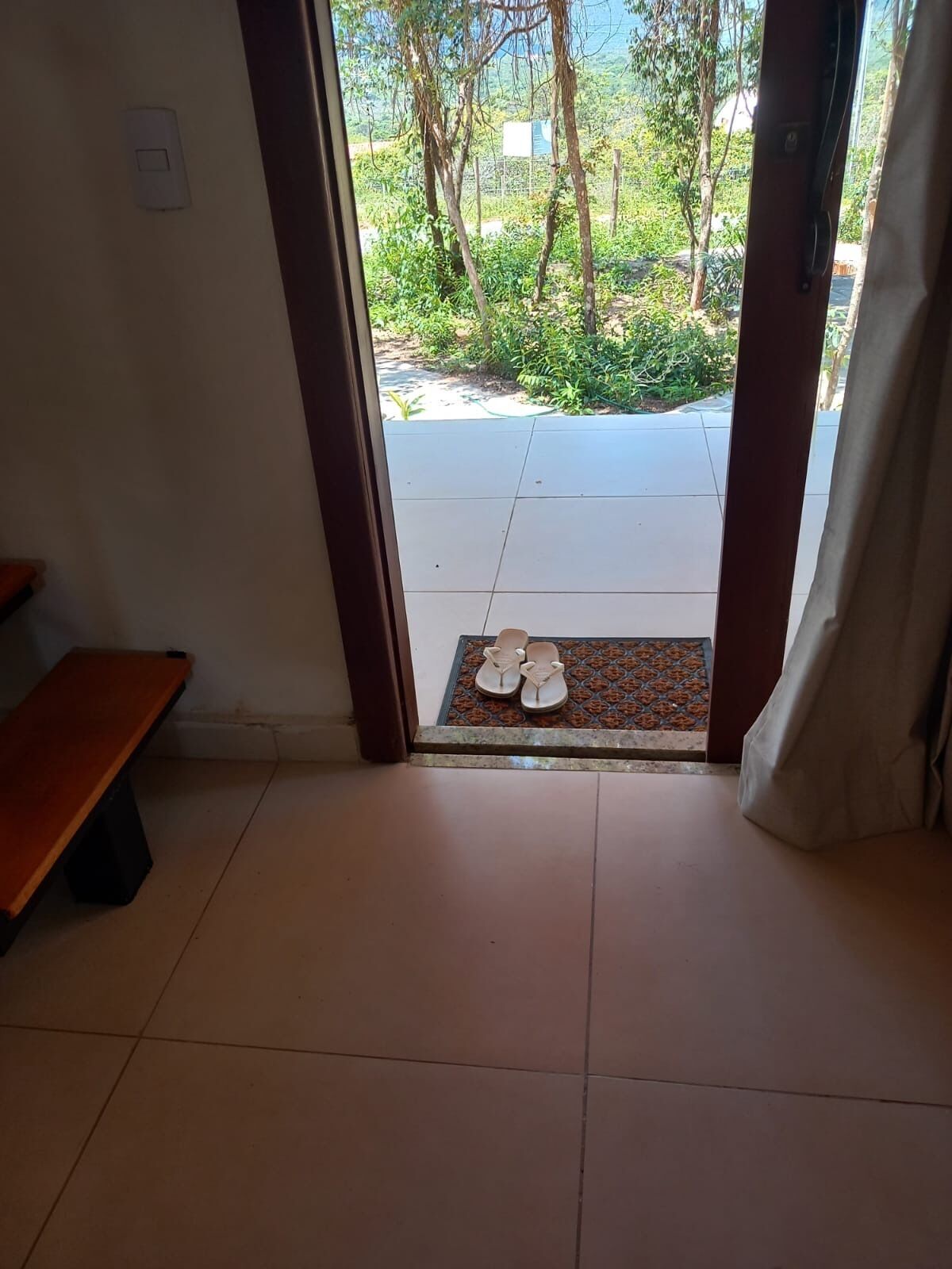 An entrance with a bench, a tiled floor, and a view of a garden through the doorway.