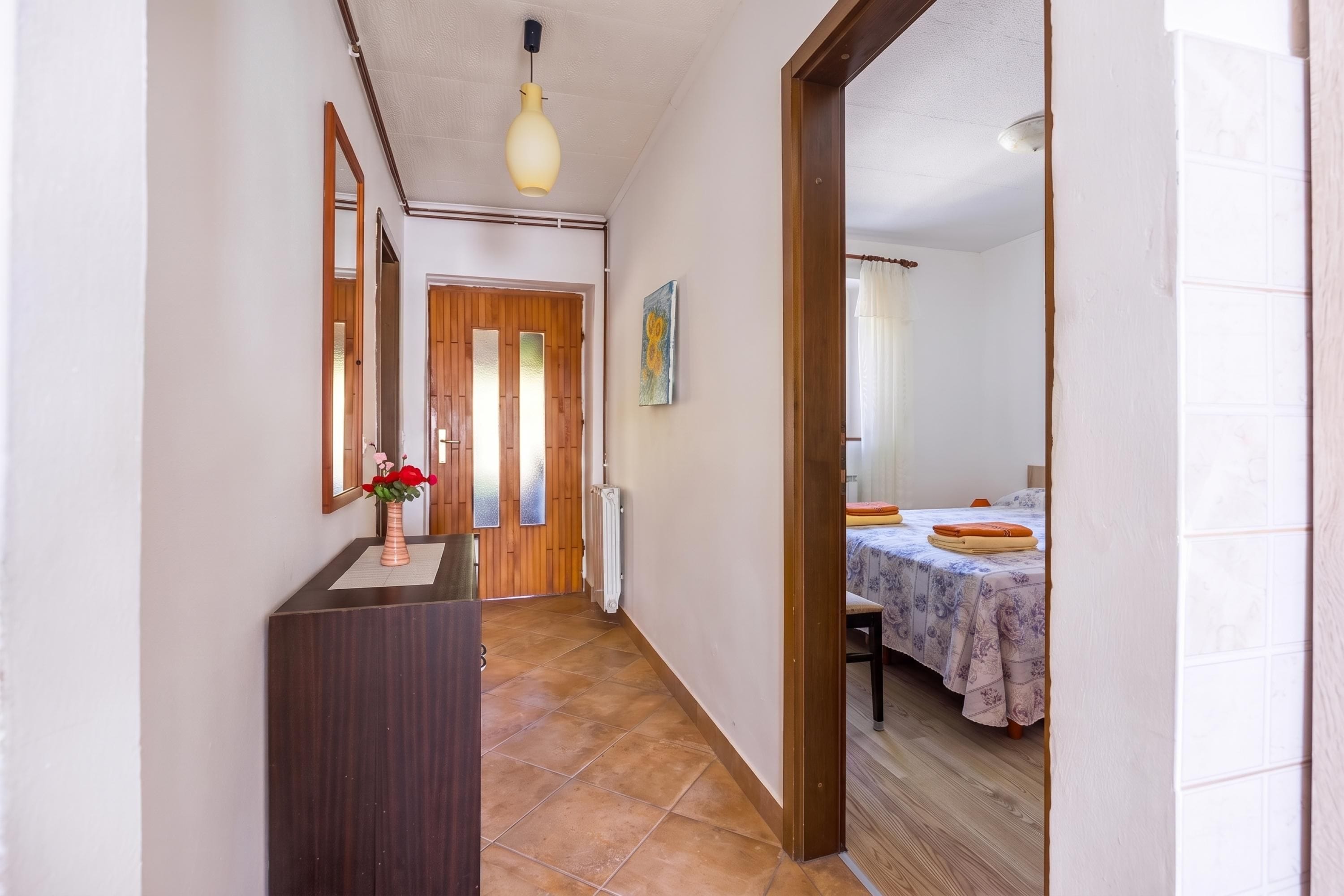 A hallway leading to a bedroom with a bed, a bedside table, and a mirror.