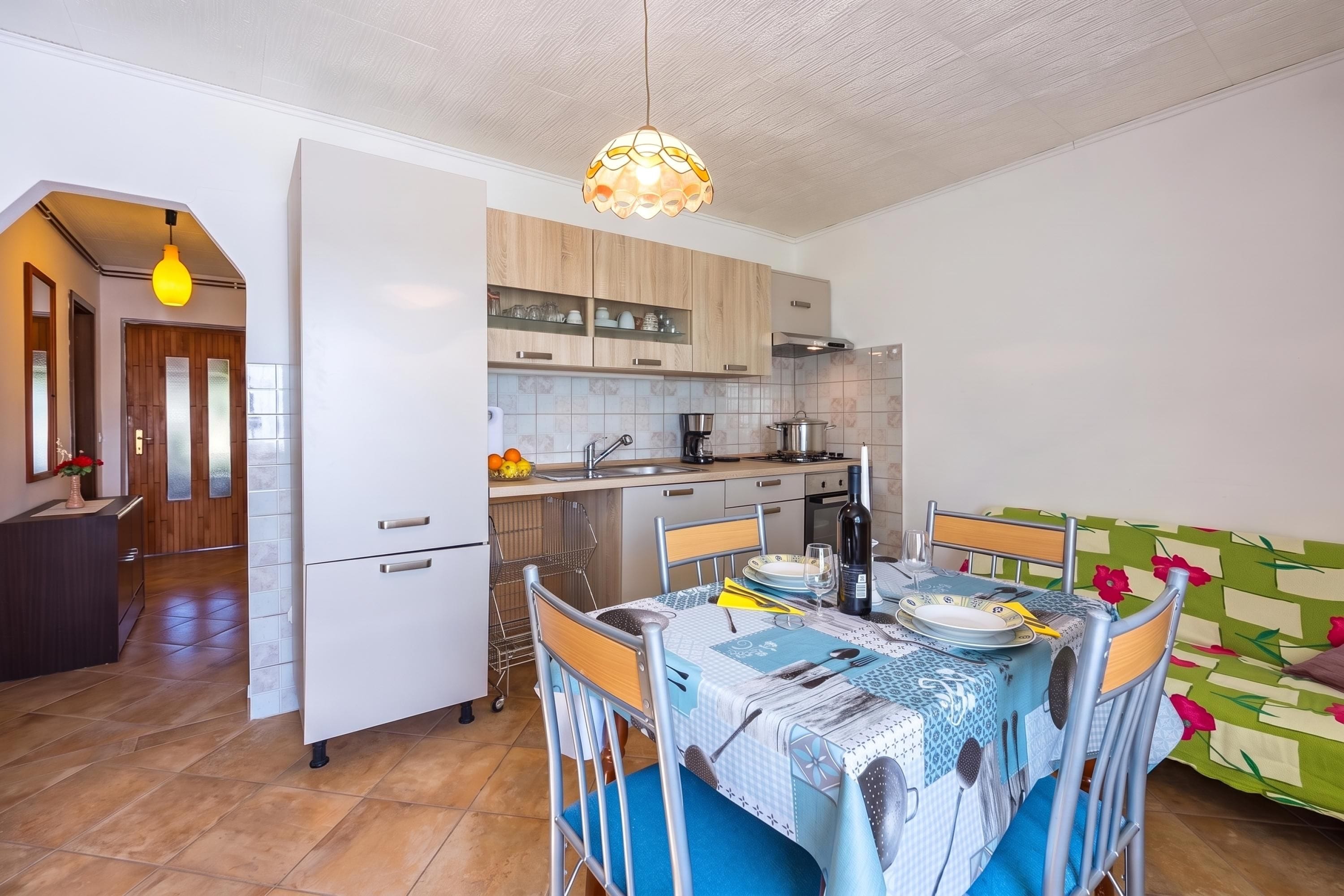 Cocina compacta con electrodomésticos modernos, comedor con mesa lista para dos personas y una zona de estar acogedora con un cojín colorido.