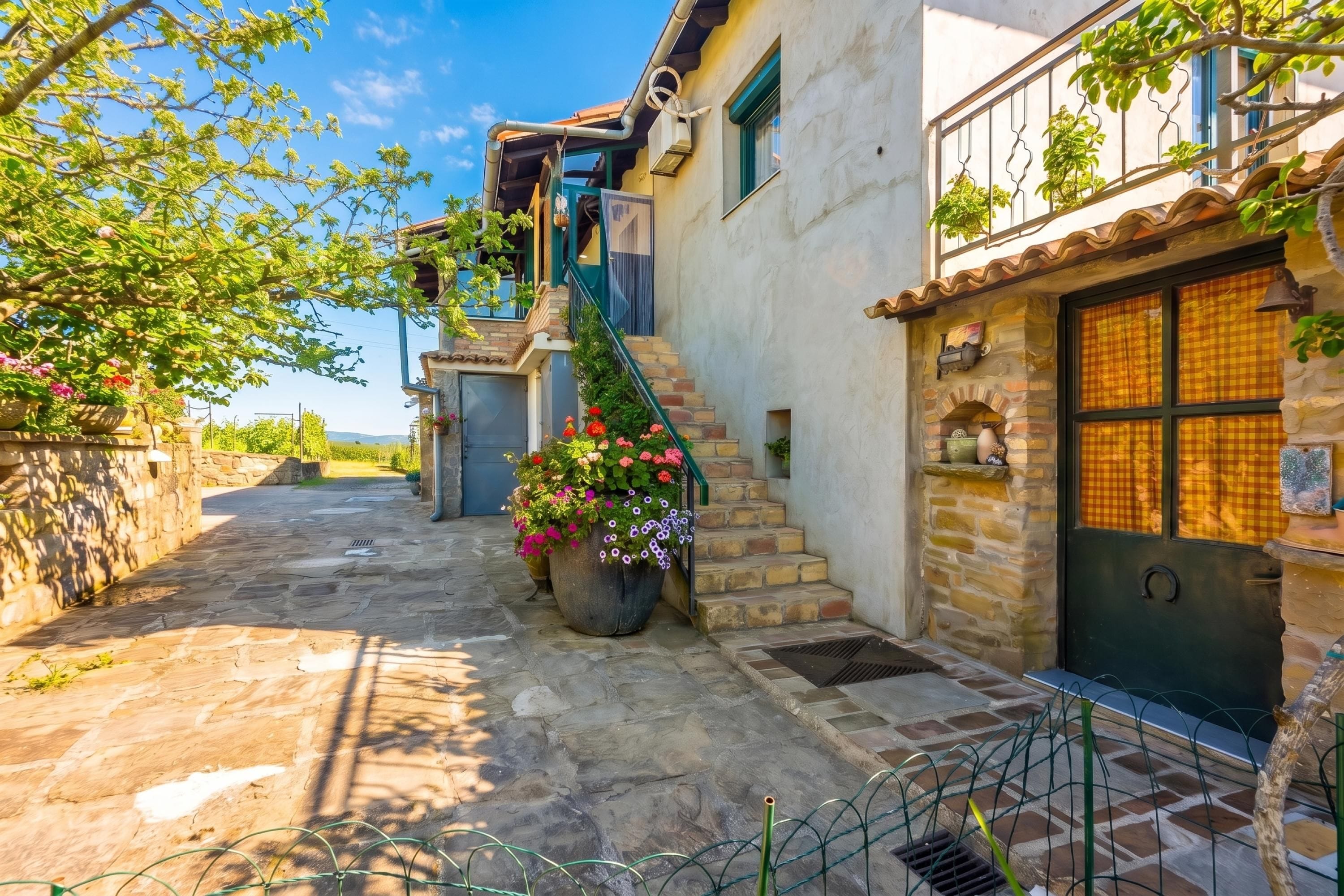 A stone building with a staircase, a large flower pot, and a metal fence.