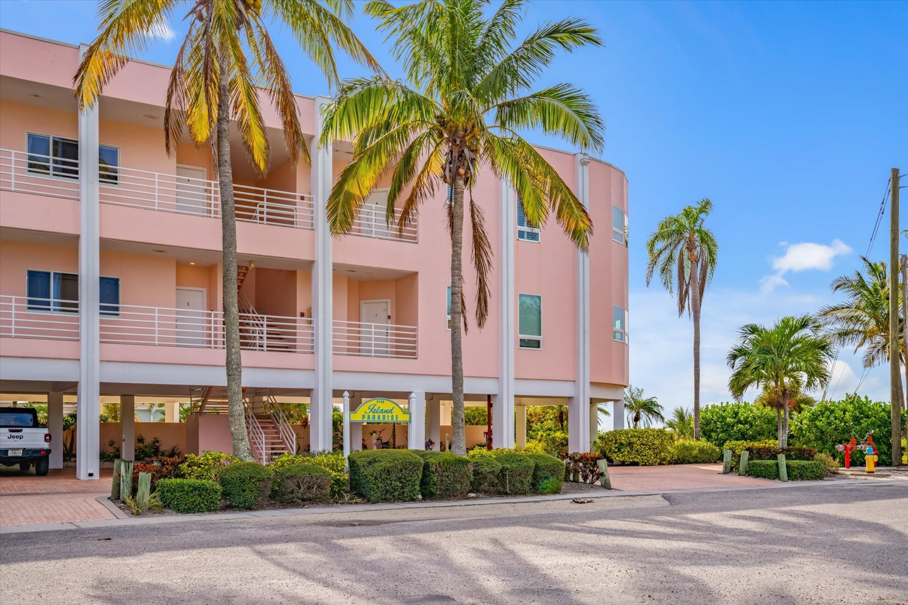 Un hotel de varios pisos con fachada rosa, palmeras y un Jeep estacionado al frente.
