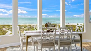 A dining area with a view of the ocean, white furniture, and a large window. - 180 Degree Ocean Views Direct Access to Holmes Beach (Holmes Beach)