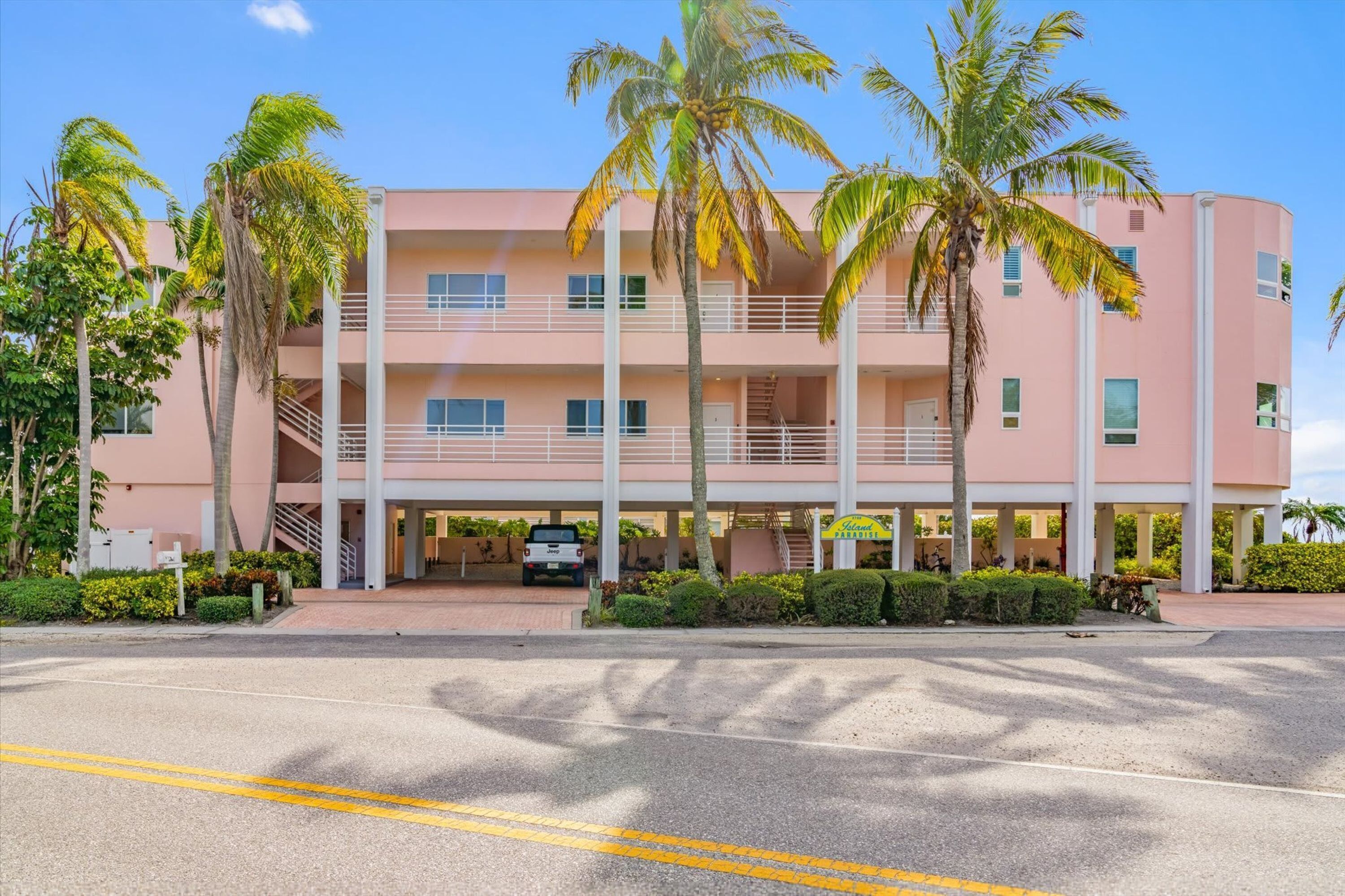 A multi-story hotel with a pink facade, palm trees, and a clear sky.
