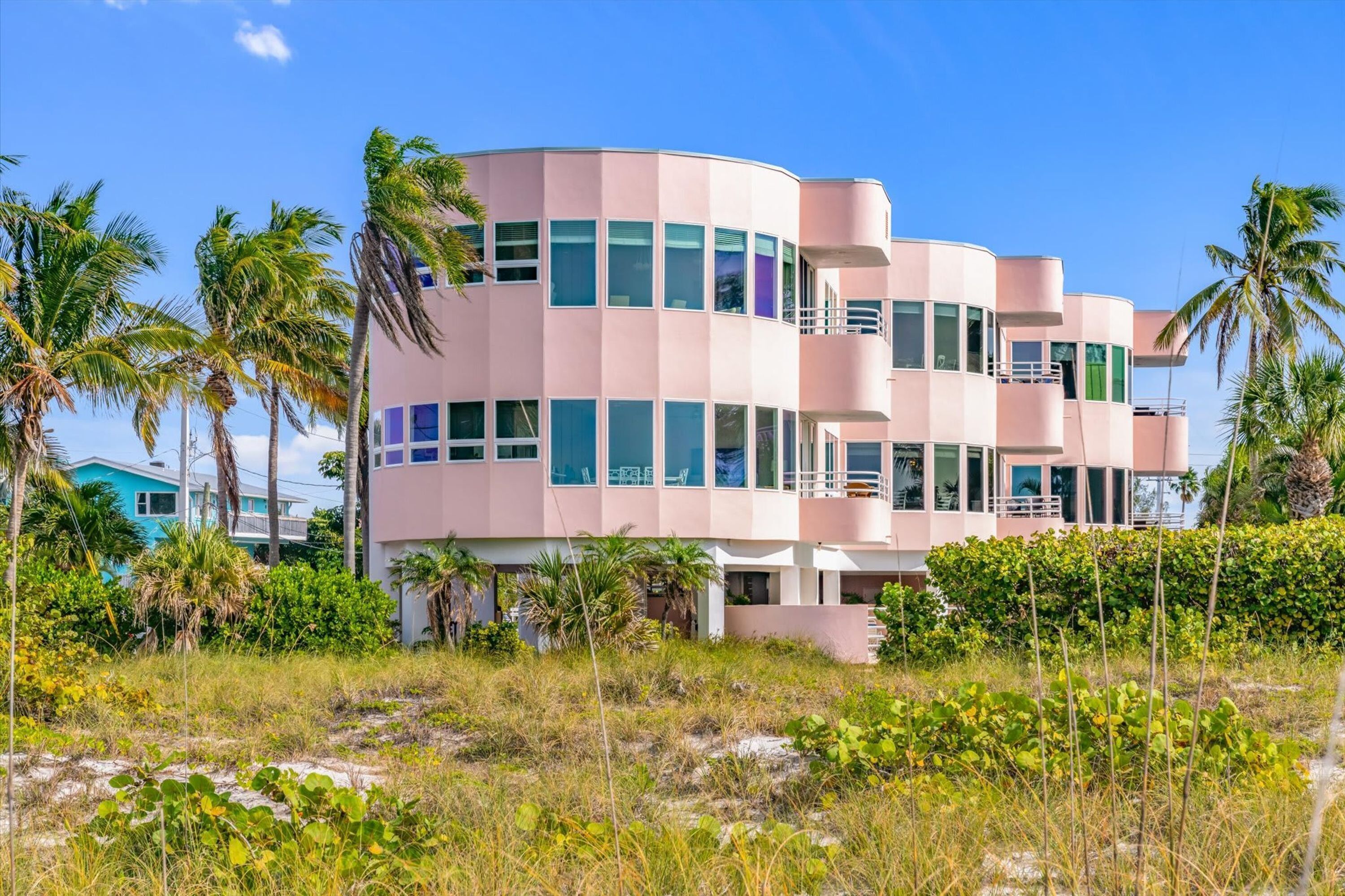 A pink multi-story building with balconies, surrounded by palm trees and vegetation.