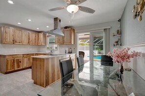 A modern kitchen with wooden cabinets, a glass dining table, and a ceiling fan. - Waterfront 3B Free Boat Parking Near Downtown (Fort Myers)