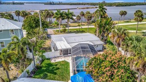 A residential property with a large glass-enclosed pool, a metal roof, and a view of a lake with palm trees. - Waterfront 3B Free Boat Parking Near Downtown (Fort Myers)