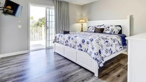 Ein Schlafzimmer mit einem Bett, einem Deckenventilator, einem an der Wand montierten Fernseher und einer Tür, die auf einen Balkon führt.