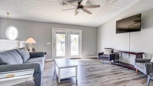Ein geräumiges Wohnzimmer mit einem grauen Sofa, einem weißen Couchtisch und einem an der Wand befestigten Fernseher.