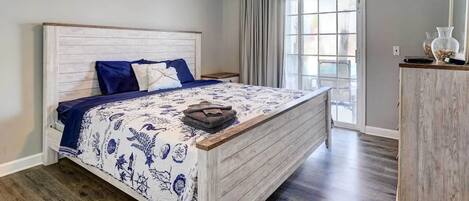 A bedroom with a wooden headboard, a bed with a patterned bedspread, a ceiling fan, a window with curtains, and a wooden dresser.