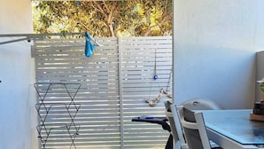 Un'area patio con tavolo e sedie, un piccolo prato verde e una recinzione bianca.