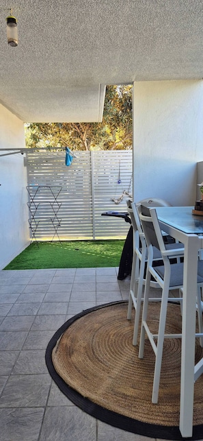 Un espace extérieur aménagé avec une table et des chaises, une petite pelouse verdoyante et une clôture blanche.