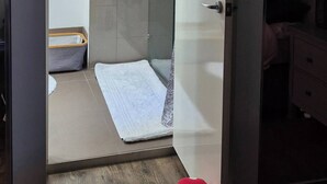 Una stanza con un letto, un comodino, una cassettiera, uno specchio e una porta che dà su un bagno con un asciugamano appeso al muro.