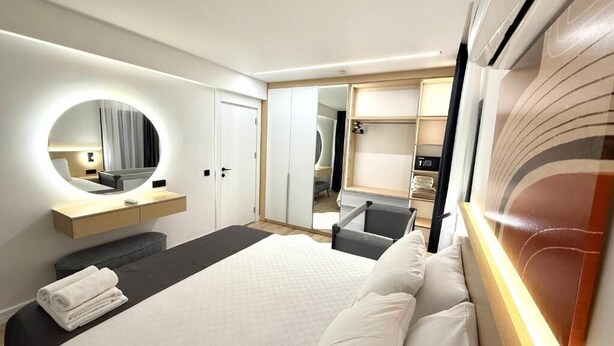 A hotel room with a bed, a bedside table, a mirror, a wardrobe, and a seating area with a chair and a table.