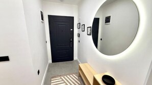 A hallway with a black door, a round mirror, a wooden bench, and a patterned rug.