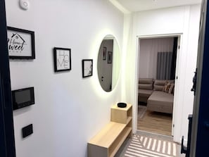 Moderni eteinen, jossa on konsolipöytä, seinälle asennettu televisio ja kehystettyjä taideteoksia.