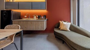 Une petite cuisine équipée avec un réfrigérateur intégré, un coin repas avec une table et des chaises, et un canapé avec des coussins.