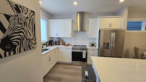 A modern kitchen with white cabinets, a stainless steel refrigerator, and a microwave. - Brand new 4-bedroom+Den main floor unit in quiet Creekview community, SW Calgary (Calgary)