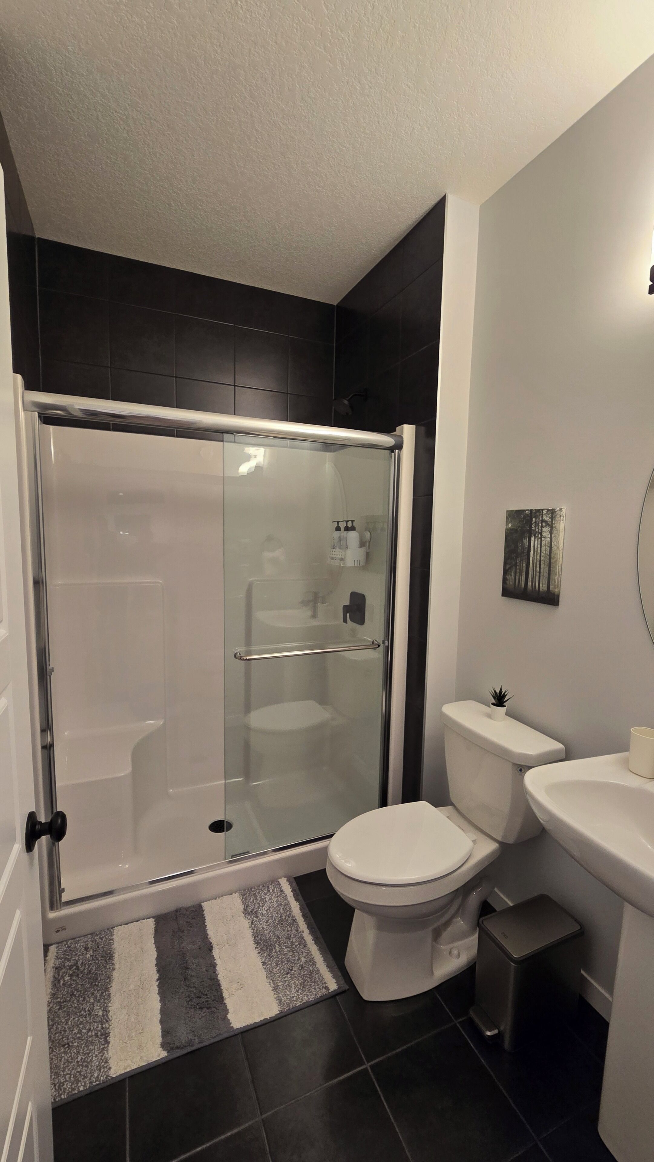 Ein modernes Badezimmer mit einer Duschkabine, einer Toilette, einem Waschbecken und einer kleinen Mülleimer.