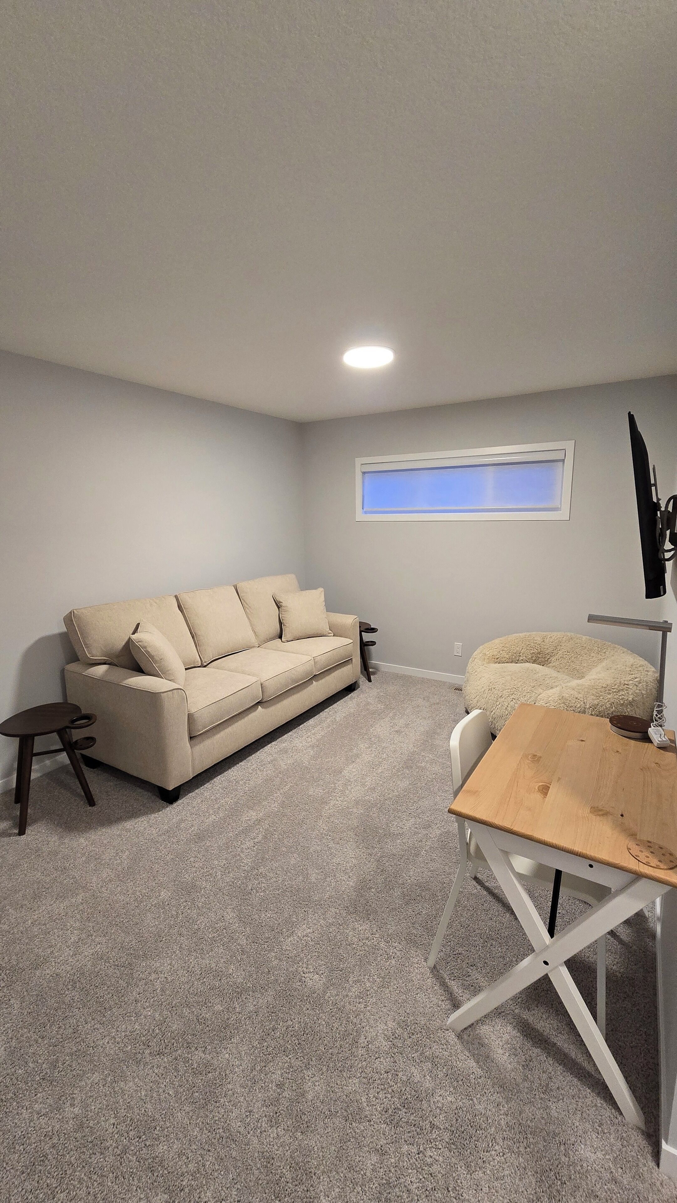 Ein Zimmer mit einem beigen Sofa, einem kleinen Holztisch, einem Fenster mit Blick und einer Deckenleuchte.