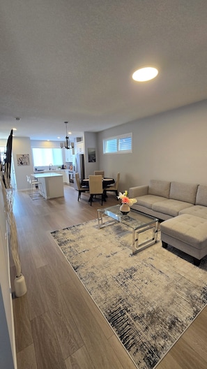 A modern living room with a sofa, a coffee table, and a dining area with chairs and a table. - Brand new 4-bedroom+Den main floor unit in quiet Creekview community, SW Calgary (Calgary)