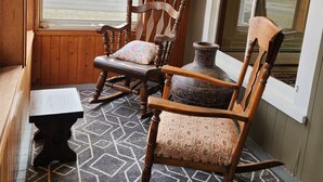 Eine Holzveranda mit zwei Schaukelstühlen, einer Bank und einem Tisch.