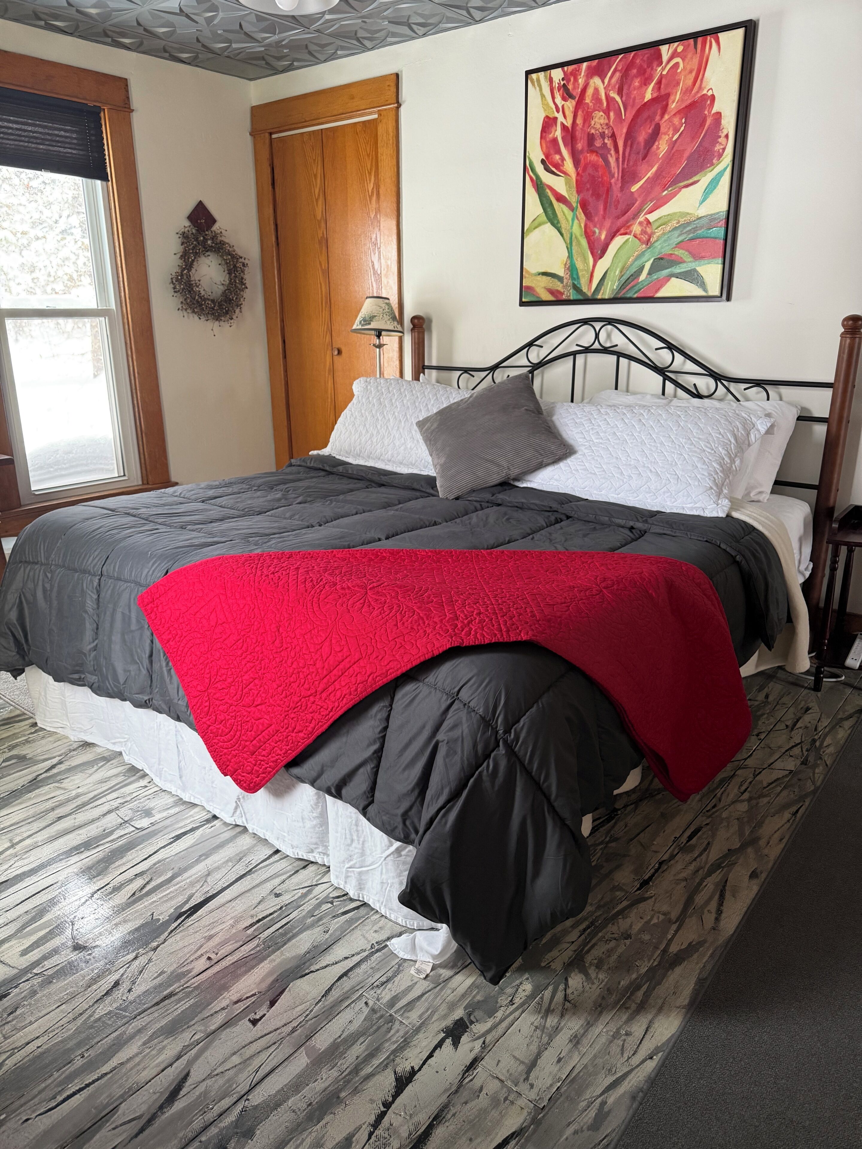 Una cama con una colcha roja, un edredón gris y negro, y almohadas blancas.
